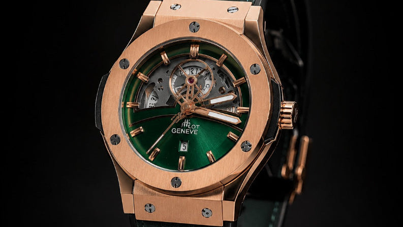 Hublot Big Bang wristwatch with a green leather strap, rose gold case, and green dial, displayed on a black Hublot box against a black background.
