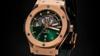 Hublot Big Bang wristwatch with a green leather strap, rose gold case, and green dial, displayed on a black Hublot box against a black background.